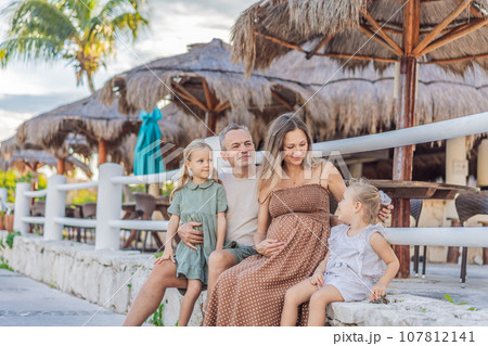 A happy, mature couple over 40 with their two daughters, enjoying a leisurely walk in a park, their joy evident as they embrace the journey of pregnancy later in life 107812141