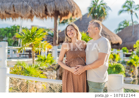 A happy, mature couple over 40, enjoying a leisurely walk in a park, their joy evident as they embrace the journey of pregnancy later in life 107812144