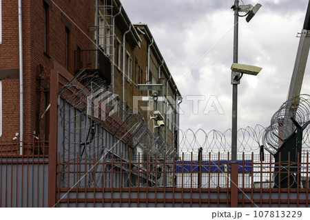 barb wire and surveillance cameras over fence in city near red brick building wall at summer day barb wire and surveillance cameras over fence in city near red brick building wall at summer day 107813229