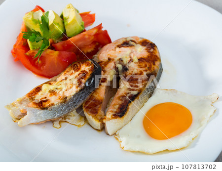 Fried salmon on white plate with fried egg, tomatoes, avocado Fried salmon on white plate with fried egg, tomatoes, avocado 107813702
