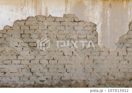 old adobe building wall with peeled off plaster 107813912