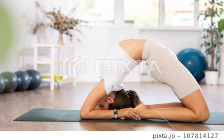 Young woman yoga trainer performing camel pose on black rug 107814127