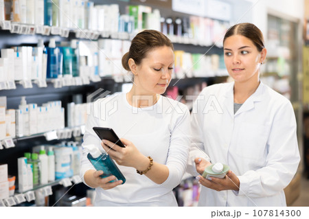 Young woman scans QR code on gel pack while friendly salesperson offers hand cream 107814300
