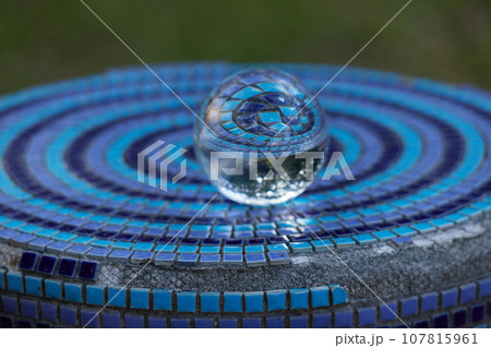 公園のセラミックタイルの台に置いてある透明な水晶ガラスボールの風景 107815961