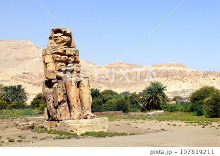 One of the famous Colossi of Memnon, Valley of Kings, Luxor, Egypt. Ancient stone statue of Pharaoh Amenhotep III in Theban Necropolis One of the famous Colossi of Memnon, Valley of Kings, Luxor, Egypt. Ancient stone statue of Pharaoh Amenhotep III in Theban Necropolis 107819211