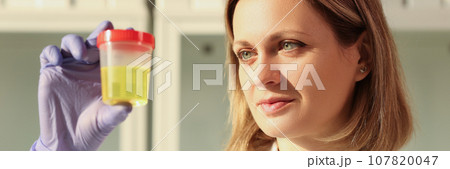 Concentrated woman looks at urine sample in container 107820047