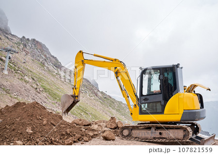 Excavator works in the highlands. Makes a trench for communications. water and electricity. in the gorge of the mountains. repair and expansion of a road Excavator works in the highlands. Makes a trench for communications. water and electricity. in the gorge of the mountains. repair and expansion of a road 107821559