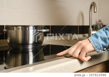 Unrecognizable woman turns on electric stove with touch control 107822086