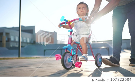 father teaches son baby to ride a children bike. happy family kid dream concept. baby baby rides a bike dad helps. father's day concept. child playing lifestyle riding a bike outdoors father teaches son baby to ride a children bike. happy family kid dream concept. baby baby rides a bike dad helps. father's day concept. child playing lifestyle riding a bike outdoors 107822604