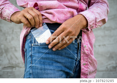 A bag of white powder taking out from the trouser pocket. Addiction and illegal trade concept A bag of white powder taking out from the trouser pocket. Addiction and illegal trade concept 107823285
