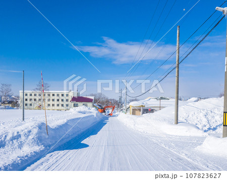 雪道の遠くで町中の除雪をするショベルカー (北海道、ニセコ町) 雪道の遠くで町中の除雪をするショベルカー (北海道、ニセコ町) 107823627