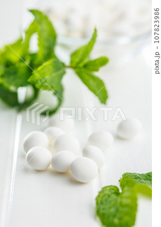 Mint candies. Menthol bonbons and mint leaves on white table. 107823986