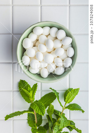 Mint candies in bowl. Menthol bonbons and mint leaves on white table. Top view. 107824008