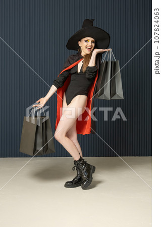 Full length portrait of young woman in black hat and coat with shopping bags . Halloween sale. Black Friday. Seasonal discounts 107824063