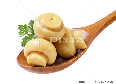 Canned mushrooms in a wooden spoon with parsley leaves close-up on a white background. Canned mushrooms in a wooden spoon with parsley leaves close-up on a white background. 107825230