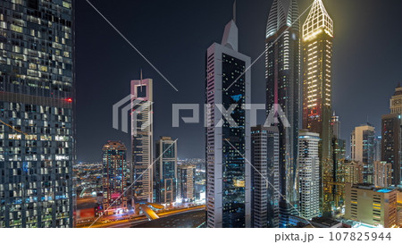 Panorama showing aerial view of Dubai International Financial District with many skyscrapers night timelapse. 107825944