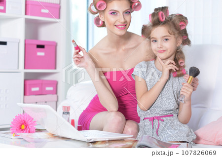 Mom and little daughter with hair curlers applying make up 107826069
