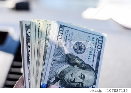 man hands over money in a car. A wad of dollars in his hand. man hands over money in a car. A wad of dollars in his hand. 107827136