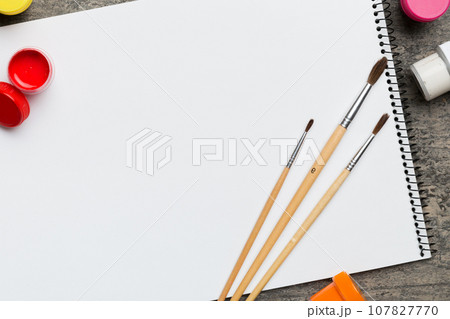 Album pages and paints, pencils, brush on a colored background. Top view with empty space. workplace for creativity. home teaching concept drawing Album pages and paints, pencils, brush on a colored background. Top view with empty space. workplace for creativity. home teaching concept drawing 107827770