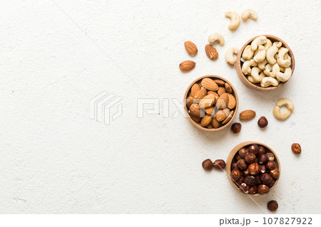 Assortment of nuts in wooden bowl on colored table. Cashew, hazelnuts, walnuts, almonds. Mix of nuts Top view with copy space 107827922