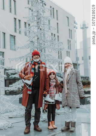 Seniors with their granddaughter at outdoor ice skating rink during winter day. 107828019