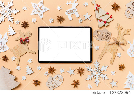 Festive decorations and toys on orange background. Top view of digital tablet. Merry Christmas concept 107828064