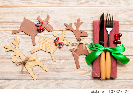 Top view of new year utensils on napkin with holiday decorations and reindeer on wooden background. Close up of christmas dinner concept 107828126