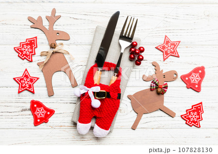 Top view of new year utensils on napkin with holiday decorations and reindeer on wooden background. Close up of christmas dinner concept 107828130