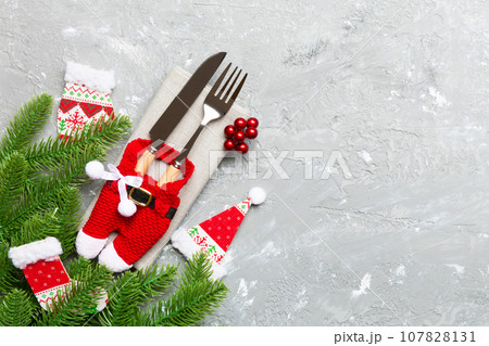 Top view of christmas decorations on cement background. Fork and knife on napkin tied up with ribbon and empty space for your design. New year pattern concept Top view of christmas decorations on cement background. Fork and knife on napkin tied up with ribbon and empty space for your design. New year pattern concept 107828131