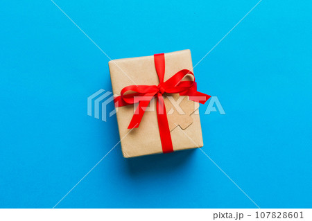 wrapped christmas or other holiday handmade present in paper with colored ribbon. Present box, decoration of gift on colourfull table, top view with copy space wrapped christmas or other holiday handmade present in paper with colored ribbon. Present box, decoration of gift on colourfull table, top view with copy space 107828601