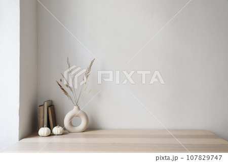 Elegant moody Scandinavian interior. Vase with dry grass bouquet, old books and little white pumpkins. Empty wall background. Modern living room, home office. Minimal autumn decor in cozy apartment. 107829747