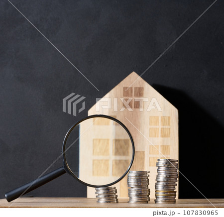 Wooden house, stack of coins, and a magnifying glass, representing the concept of real estate purchase, rental growth, and mortgage interest 107830965