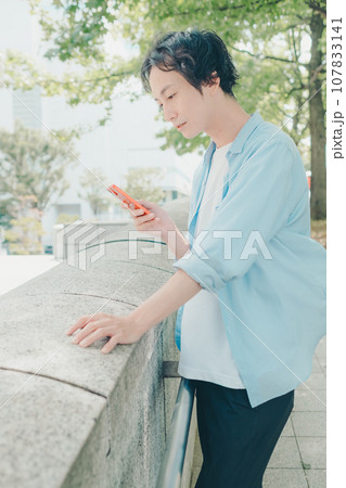 都会の街並みでスマートフォンを触る30代男性 107833141