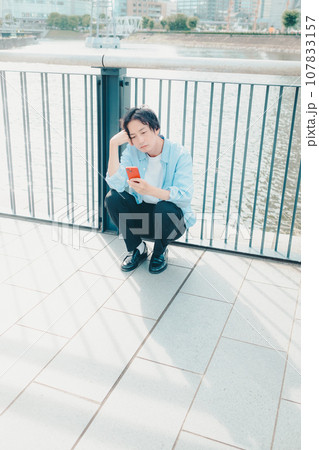 都会の街並みでスマートフォンを触る30代男性 107833157