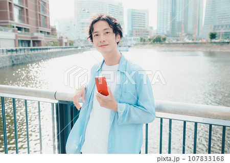 都会の街並みでスマートフォンを触る30代男性 107833168