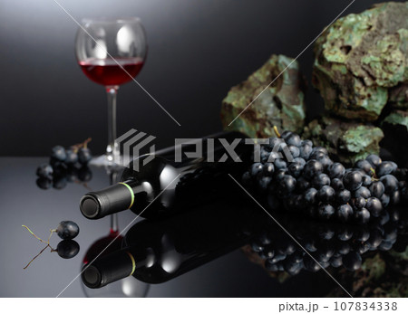 Blue grapes and red wine on a black reflective background. 107834338