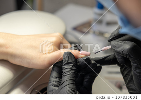 Female hands and tools for manicure, process of performing manicure in beauty salon. Nail care procedure in a beauty salon. Gloved hands of an experienced manicurist in gloves are varnished nails 107835001
