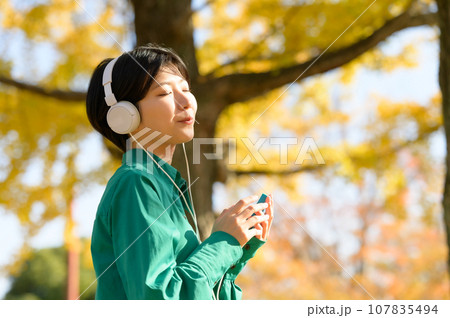 秋晴れの公園で音楽を楽しむ女性 107835494
