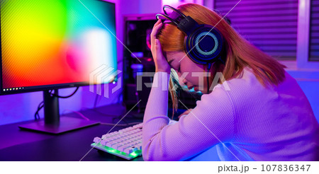 Game over you lose. Angry Asian gamer wearing gaming headphones playing joystick console video game on computer PC neon light at home feeling sad disappointed about game losing, player unhappy E-Sport 107836347