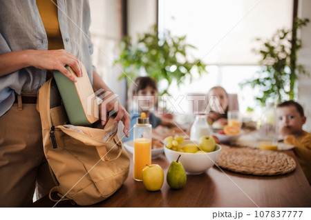 Mother packing school snacks for her children into school bag. Snack, school lunch in a snack box for school. 107837777
