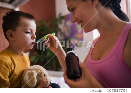Young mother giving medicines, coughing syrup from spoon to her sick little son. Concept of children seasonal illness, viruses and kid's immune system. 107837795