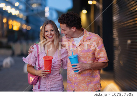 Gen Z couple in pink outfits leaving the cinema with drinks in hand. The young zoomers watched movie addressing topic of women, her position in world, and body image. Gen Z couple in pink outfits leaving the cinema with drinks in hand. The young zoomers watched movie addressing topic of women, her position in world, and body image. 107837908