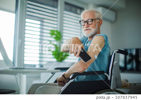 Diabetic senior man checking blood glucose level using continuous glucose monitor. Elderly man connecting CGM with smarphone to see blood sugar levels in real time. 107837945