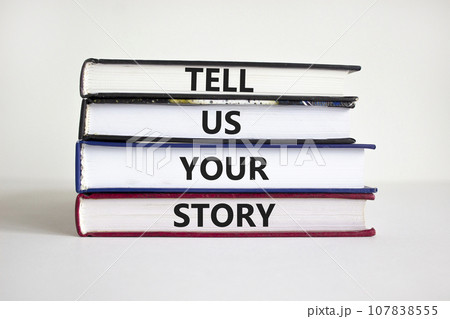 Tell us your story symbol. Books with words 'Tell us your story'. Businessman hand. Beautiful white background, copy space. Business, storytelling and tell us your story concept. Tell us your story symbol. Books with words 'Tell us your story'. Businessman hand. Beautiful white background, copy space. Business, storytelling and tell us your story concept. 107838555