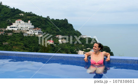 Happy young Caucasian woman resting in infinity pool by the blue sea Happy young Caucasian woman resting in infinity pool by the blue sea 107838601