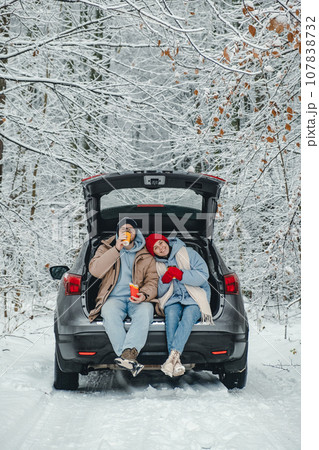 A couple in a snowy forest stopped for a drink and snack and a rest from the road A couple in a snowy forest stopped for a drink and snack and a rest from the road 107838732