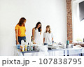 Cute teenager in white T-shirt and two women in casual clothes are checking out acrylic-painted work. Young artist communicates with teachers in art workshop. 107838795