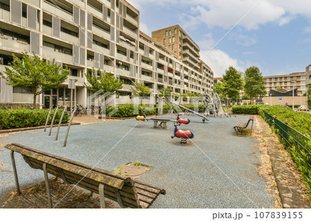 an empty playground area in the middle of a large apartment building with several children playing on swings and swing equipment 107839155