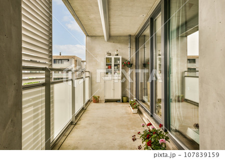a balcony with flowers in the window sis and an open door leading out to the outside space, on a sunny day 107839159
