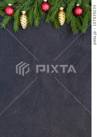 Christmas or New Year border background with Christmas tree branches on a dark textured background and red glass balls decoration. Fir branches, spruce pine cones. Top view with copy space 107839235